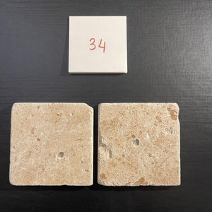 May include: Two beige square tiles with a rough, textured surface. The tiles have a light brown color with small, darker brown flecks throughout. The tiles are arranged side-by-side.