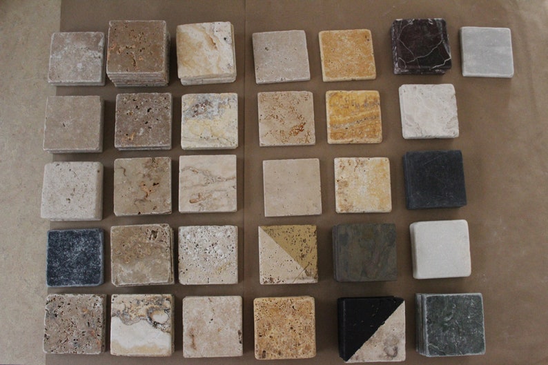 May include: Assortment of small square tiles in various shades of beige, brown, gray, and black. Some tiles have a textured surface, while others are smooth. The tiles are arranged in a grid pattern on a brown surface.