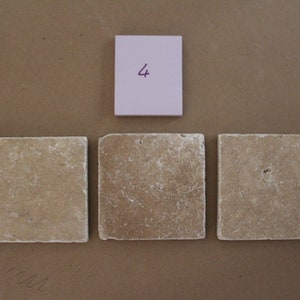 May include: Three beige square tiles with a rough texture. A pink sticky note with the number "4" written on it is above the tiles.