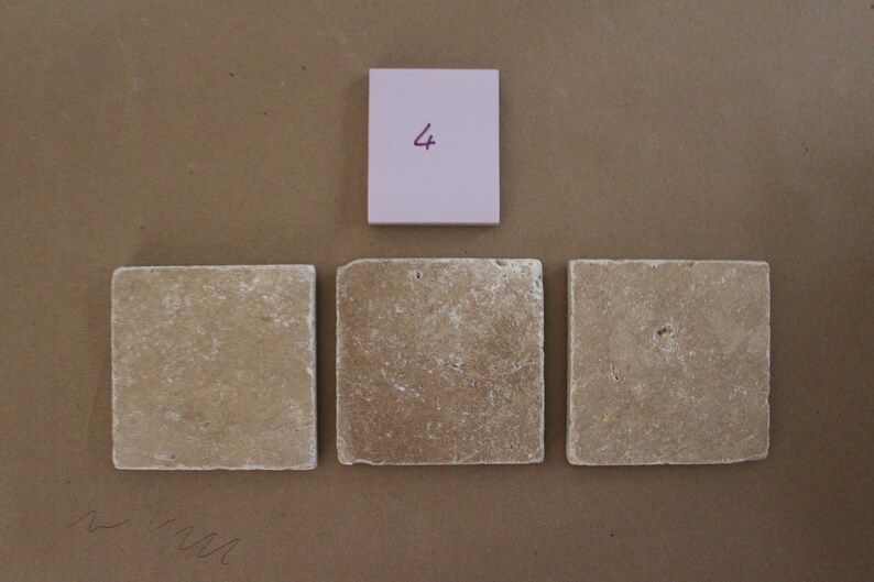 May include: Three beige square tiles with a rough texture. A pink sticky note with the number "4" written on it is above the tiles.