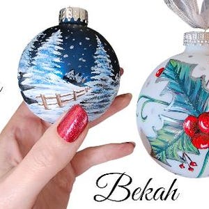 May include: Three hand-painted Christmas ornaments. One ornament is blue with a white tree and snowflakes. Another ornament is white with green holly and red berries. The third ornament is red with green holly and the letters "JOY" in white.