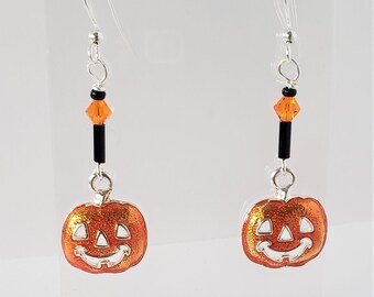 May include: A pair of Halloween-themed earrings. Each earring features a smiling orange pumpkin charm with a silver-colored hook. The design includes black and orange beads, creating a festive accessory.