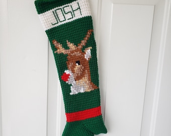 May include: A green, white, and red Christmas stocking with the name "JOSH" embroidered in white. The stocking features a reindeer design. It is hanging on a white door.
