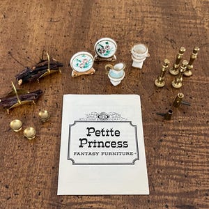 May include: A collection of miniature dollhouse furniture and accessories, including small chairs, a toilet, and brass fixtures. A card with the text "Petite Princess Fantasy Furniture" is also present. The items are arranged on a wooden surface.