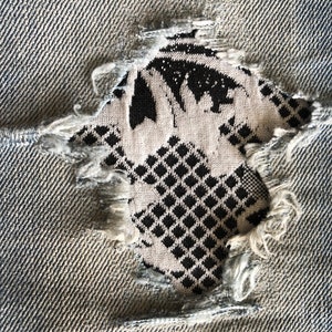 May include: A close-up of a ripped pair of blue jeans with a black and white patterned fabric showing through the hole.