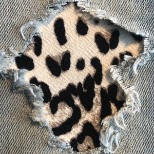 Peut inclure: Gros plan sur un jean bleu déchiré avec un patch en tissu imprimé animal noir et blanc cousu dans le trou.