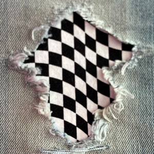 May include: A black and white checkered pattern peeking through a ripped hole in a pair of gray denim jeans.