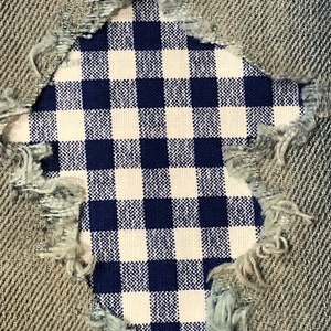 May include: A close-up of a blue and white gingham fabric patch sewn over a hole in a pair of denim jeans.