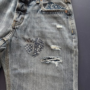 May include: Distressed denim jeans with a bandana print heart patch and a smaller bandana patch on the right leg.
