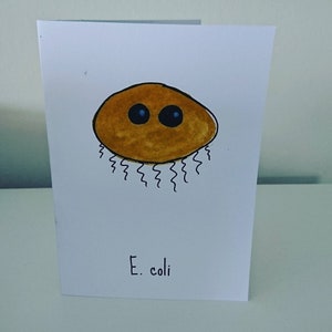 Pode incluir: Uma ilustração desenhada à mão de uma bactéria E. coli castanha com dois olhos azuis. A bactéria é desenhada em um estilo simples e de desenho animado.