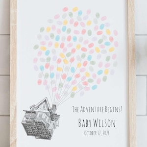 Puede incluir: Impresi&oacute;n enmarcada con un marco de madera clara. La impresi&oacute;n presenta una casa con globos de huellas dactilares de colores y el texto "The Adventure Begins!" con el nombre y la fecha de un beb&eacute;. El fondo es blanco.