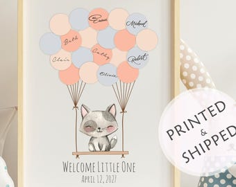 May include: A framed print with a raccoon illustration in a swing, held up by pastel balloons. The balloons are peach, blue, and grey. The text "Welcome Little One" and the date April 12, 2021, are below the raccoon illustration. Names are written on the balloons.