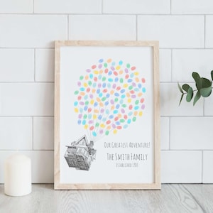Puede incluir: Una impresi&oacute;n enmarcada con un marco de madera clara. La obra de arte presenta una casa levantada por huellas dactilares coloridas, que se asemejan a globos. El texto dice: "Our Greatest Adventure! The Smith Family Established 1900."