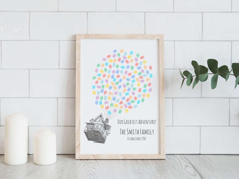 Puede incluir: Una impresi&oacute;n enmarcada con un marco de madera clara. La obra de arte presenta una casa levantada por huellas dactilares coloridas, que se asemejan a globos. El texto dice: "Our Greatest Adventure! The Smith Family Established 1900."