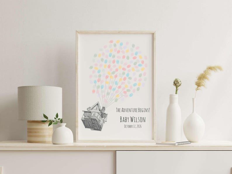 Puede incluir: Una impresi&oacute;n enmarcada con una ilustraci&oacute;n de una casa y globos de huellas dactilares de colores. El texto dice "The Adventure Begins!" y "Baby Wilson, October 17, 2026." La impresi&oacute;n est&aacute; en un estante blanco con una l&aacute;mpara y jarrones.