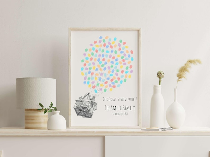 Puede incluir: Impresi&oacute;n art&iacute;stica enmarcada con una ilustraci&oacute;n de una casa unida a un grupo de huellas dactilares de colores, que se asemejan a globos. El texto dice: "Our Greatest Adventure! The Smith Family Established 1980."