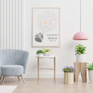 Puede incluir: Un estampado enmarcado con un dise&ntilde;o de globo aerost&aacute;tico hecho de huellas dactilares de colores. El texto dice "THE ADVENTURE BEGINS" y "BABY WILSON" con una fecha. Una silla azul claro, una mesa auxiliar y plantas completan la habitaci&oacute;n.