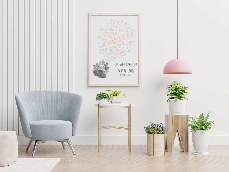 Puede incluir: Un estampado enmarcado con un dise&ntilde;o de globo aerost&aacute;tico hecho de huellas dactilares de colores. El texto dice "THE ADVENTURE BEGINS" y "BABY WILSON" con una fecha. Una silla azul claro, una mesa auxiliar y plantas completan la habitaci&oacute;n.
