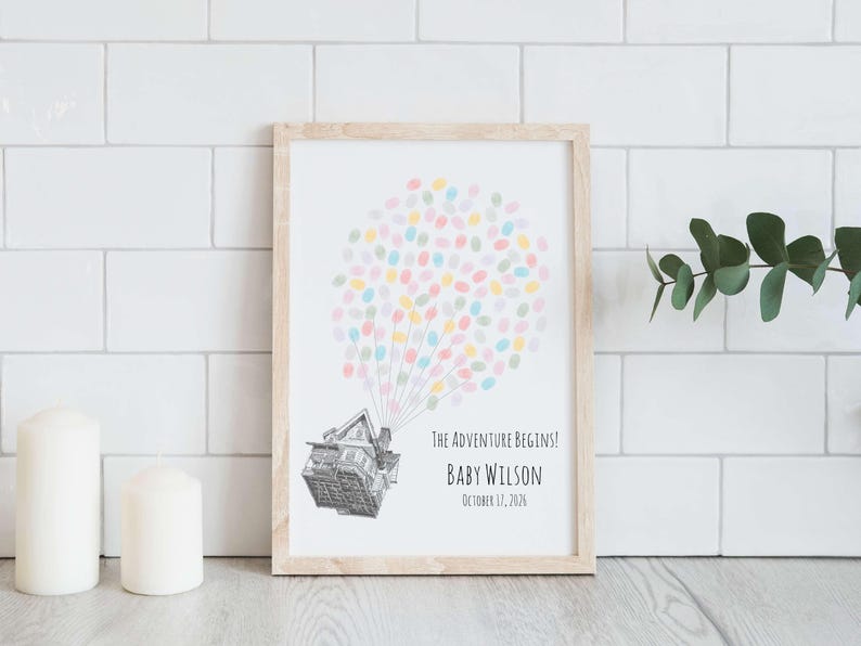 Puede incluir: Impresi&oacute;n enmarcada con un marco de madera clara. La impresi&oacute;n presenta una casa con globos de huellas dactilares de colores y el texto "The Adventure Begins!" con el nombre y la fecha de un beb&eacute;. El fondo es blanco.