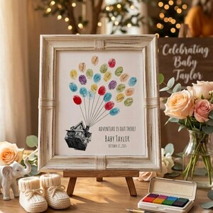 May include: A framed print in a distressed white frame featuring a black and white illustration of a house lifted by colorful fingerprint balloons. The text reads ADVENTURE IS OUT THERE! BABY TAYLOR OCTOBER 17, 2026 in a clean black sans-serif font.
