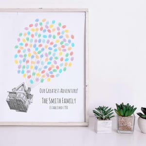 Puede incluir: Impresi&oacute;n enmarcada con una ilustraci&oacute;n de una casa y un globo de huellas dactilares de colores. El texto dice "Our Greatest Adventure! The Smith Family Established 1980." Tres peque&ntilde;as suculentas en macetas est&aacute;n frente a la impresi&oacute;n.