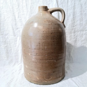 May include: A brown stoneware jug with a handle. The jug has a speckled glaze and a rounded body.