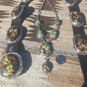 May include: A turquoise and silver necklace and belt set with a southwestern design. The necklace has five turquoise stones and the belt has four turquoise stones.