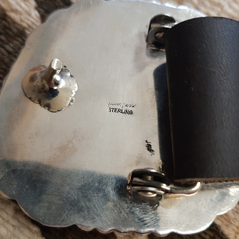 May include: Silver belt buckle with a detailed design. The back of the buckle is stamped with "sterling" and "Indian Jewelry".