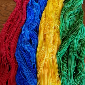 Puede incluir: Cuatro ovillos de hilo en rojo, azul, amarillo y verde. El hilo est&aacute; dispuesto en una pila vertical.