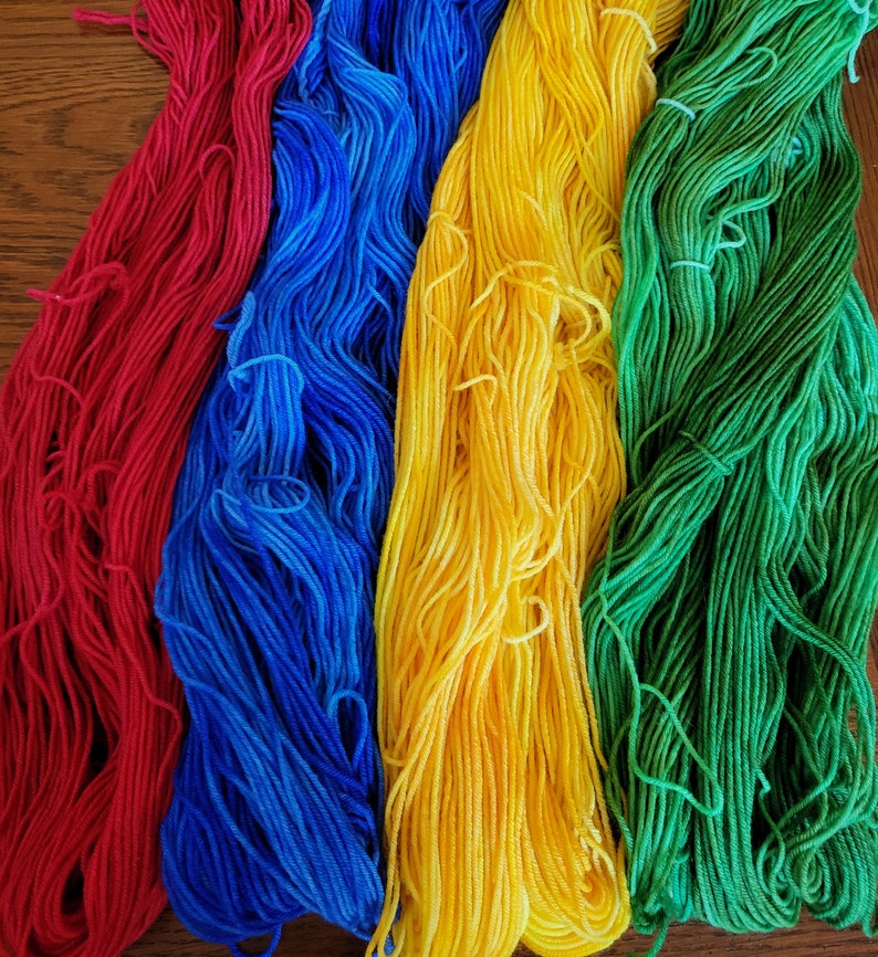 Puede incluir: Cuatro ovillos de hilo en rojo, azul, amarillo y verde. El hilo est&aacute; dispuesto en una pila vertical.