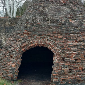 Puede incluir: Una gran estructura c&oacute;nica de ladrillo con un exterior desgastado de color rojo oscuro y marr&oacute;n, con juntas de mortero visibles y una amplia abertura arqueada en la base. La estructura est&aacute; construida con ladrillos envejecidos.