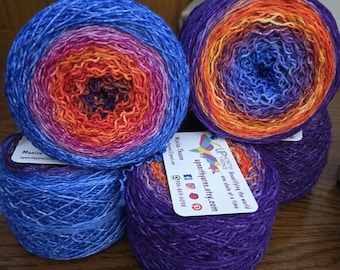 Op de afbeelding: Een verzameling kleurrijke garenballen in tinten blauw, paars, oranje en roze. Het garen is gerangschikt in een gradiëntpatroon, waarbij elke bal een unieke kleurovergang vertoont. Elke bal heeft een label met de tekst "UPNORTH YARNS - one skein at a time".