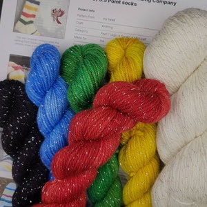 Puede incluir: Seis ovillos de hilo en varios colores, incluyendo rojo, verde, azul, amarillo, negro y blanco. Cada ovillo tiene un hilo de brillo plateado tejido a trav&eacute;s de &eacute;l. El hilo est&aacute; etiquetado como "Slouchy Hudson Bay Trading Company (HBTC) 3.5 Point socks".