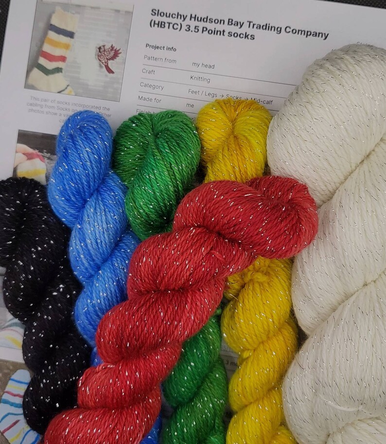 Puede incluir: Seis ovillos de hilo en varios colores, incluyendo rojo, verde, azul, amarillo, negro y blanco. Cada ovillo tiene un hilo de brillo plateado tejido a trav&eacute;s de &eacute;l. El hilo est&aacute; etiquetado como "Slouchy Hudson Bay Trading Company (HBTC) 3.5 Point socks".
