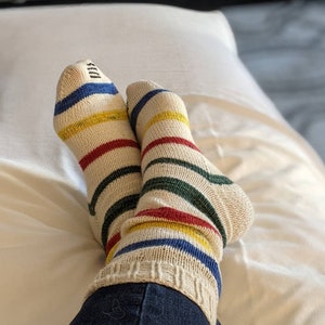 Puede incluir: Un par de calcetines a rayas con rayas rojas, amarillas, azules y verdes sobre un fondo blanco. Los calcetines se llevan puestos en los pies de una persona y la persona lleva pantalones vaqueros azules.