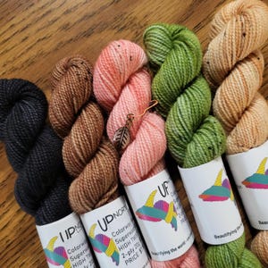 May include: Four skeins of yarn in different colors: black, brown, pink, and green. Each skein is labeled with the brand name "UDNORTH" and the text "Colorway Superwash High Twist 2-ply 209g PRICE: $15".