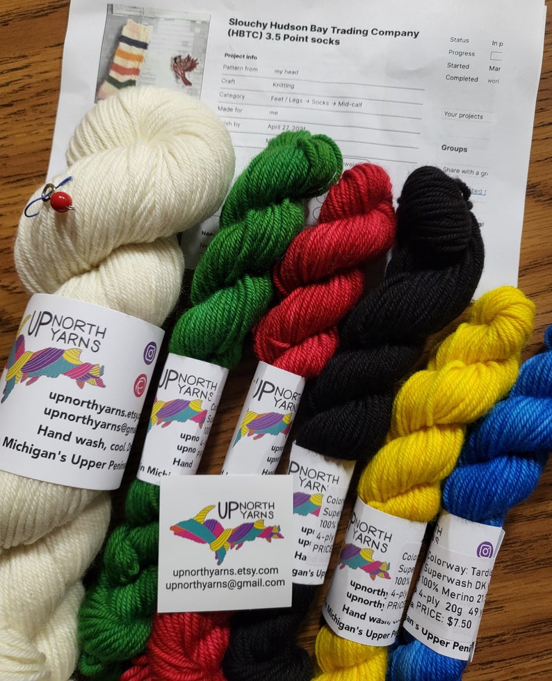 Puede incluir: Surtido de ovillos de lana de colores en verde, rojo, negro, amarillo, azul y blanco. La lana est&aacute; etiquetada con "Up North Yarns" e incluye informaci&oacute;n sobre la composici&oacute;n de la lana, su peso y las instrucciones de cuidado. La lana es adecuada para proyectos de tejido o ganchillo.