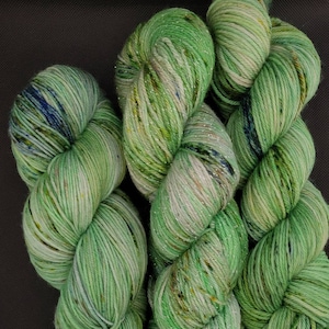 May include: Close-up of several skeins of green yarn with subtle variations in color and texture. The yarn has a soft, slightly shimmering appearance, with hints of blue and yellow. Ideal for knitting or crochet projects.