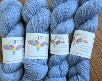 May include: Three skeins of light blue yarn with white labels that say "Up North Yarns" and include a colorful illustration of the Upper Peninsula of Michigan. The labels also say "Beautifying the world - one skein at a time. Hand wash, cool water, lay flat to dry."