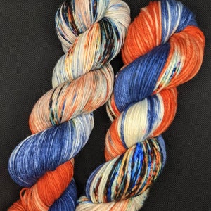 May include: Two skeins of yarn, one orange, white, and blue, and the other white, orange, and blue with black speckles.
