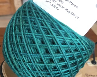 May include: A ball of teal-colored yarn with a label attached. The label reads "Colorway: Tealish Superwash 100% Merino DK High Twist 3-ply 19.5 micron 100g 246 yd". The yarn is tightly wound, showing a woven pattern.