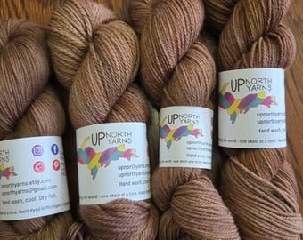May include: Three skeins of brown yarn with labels that say "Up North Yarns". The labels feature a map of Michigan and the text "upnorthyarns.etsy.com", "upnorthyarns@gmail.com", "Hand wash, cool", "Dry flat", "Hand dyed in Michigan's Upper Peninsula", and "The world - one skein at a time. Hand dyed in Michigan's Upper Peninsula."