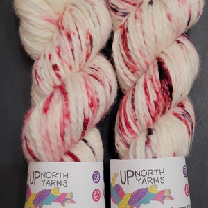 May include: Two skeins of chunky yarn in cream with red and black speckles. Each skein has a label with the text "UP NORTH YARNS" and contact information. The yarn is hand-dyed in Michigan's Upper Peninsula.