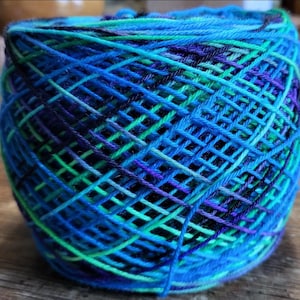 May include: A ball of yarn with a blue, green, and purple color scheme. The yarn is wound in a tight spiral.