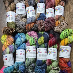 May include: A white ceramic mug with a black handle and the text "But First, Coffee" in a black, handwritten-style font. The mug is on a white surface.