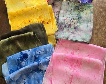 Puede incluir: Una colección de ocho pañuelos de seda en varios colores y patrones, incluyendo amarillo, rosa, azul, verde y morado. Los pañuelos están doblados y dispuestos sobre una superficie de madera.
