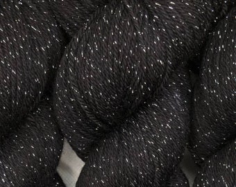 May include: A skein of black yarn featuring a consistent metallic silver thread twisted throughout the fibers. The yarn has a soft, plied texture with a distinct shimmer created by the reflective silver strands woven into the dark base material.