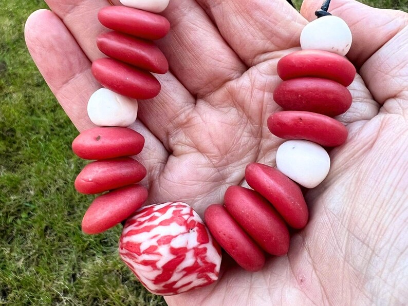 A necklace with red and white beads. The necklace is made up of smooth, oval red beads and round, white beads. A larger, patterned red and white bead is at the centre of the necklace.