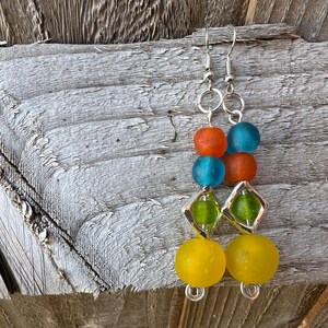 Bright and colourful drop earrings. Yellow, green, orange and blue recycled glass beads from Ghana stack on top of each other. Silver coated findings are used, including a diamond shaped frame around the green bead.