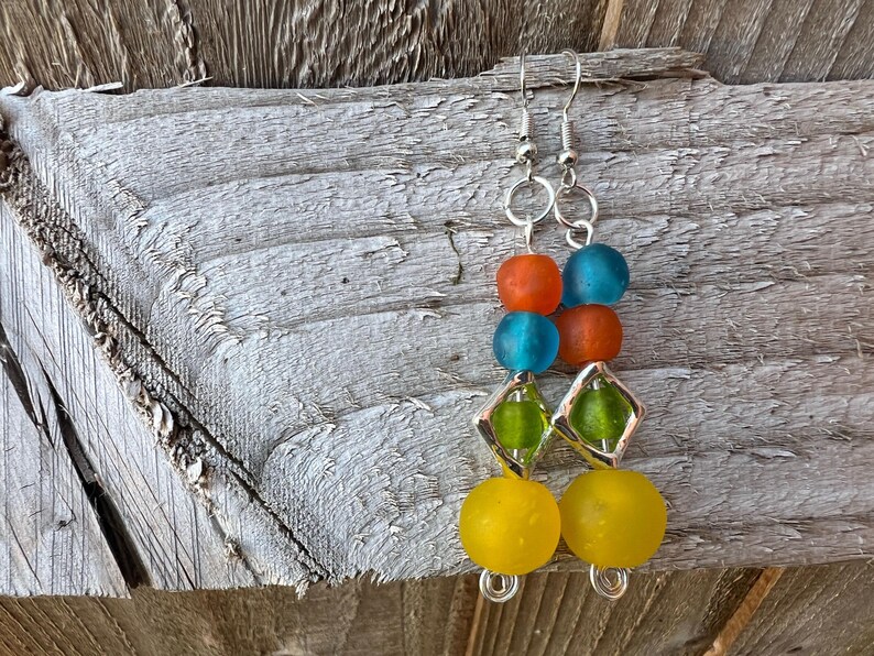 Bright and colourful drop earrings. Yellow, green, orange and blue recycled glass beads from Ghana stack on top of each other. Silver coated findings are used, including a diamond shaped frame around the green bead.